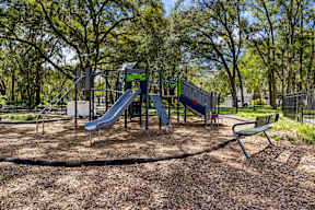 Playground with slides and bench at The Flats at Tioga Town Center apartments in Newberry, FL.
