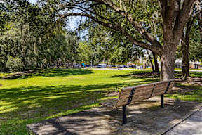 Shaded bench facing grassy common area and playground near The Flats at Tioga Town Center apartments in Newberry, FL