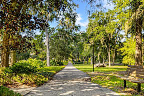 Shaded walking path with bench and lamp posts among oak trees at The Flats at Tioga Town Center.