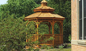 A wooden gazebo with a brown roof is surrounded by greenery.