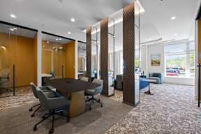 Meeting rooms with tables and chairs near a community lounge with comfortable seating and large windows.