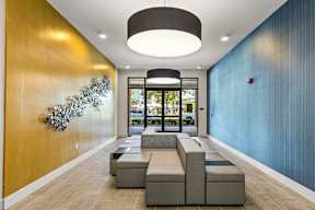 Lobby with modular gray seating, large pendant lights, yellow accent wall and metal art at The Flats at Tioga Town Center.