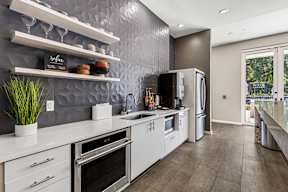 Modern community kitchen with stainless appliances and textured tile at The Flats at Tioga Town Center.