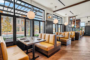 A restaurant with a long table and chairs with a view of the street outside.