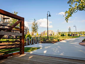 A large green space with a walking trail, path lights, trees, bike station, and bridge near River Station apartment buildings.