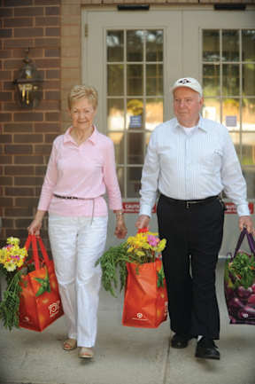 A man and a woman are walking out of a building carrying bags of groceries.