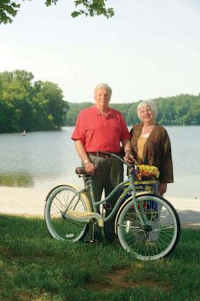 An elderly couple standing next to a green bicycle.