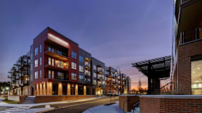 A corner street view of River Station's apartment buildings at sunset with trees and the capitol building in the background.