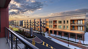 A balcony view of River Station's modern apartment building lining a street with the sun setting in the background.