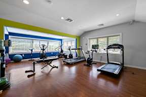 A spacious fitness center with beautiful hardwood flooring, large windows, cardio and weight equipment, a filtered water station, and large windows.