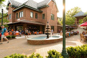 A group of people are sitting at tables under a building with a fountain in the middle of a courtyard.