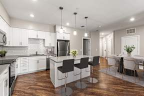 Open-plan kitchen with island, three bar stools and stainless appliances at The Flats at Tioga Town Center.