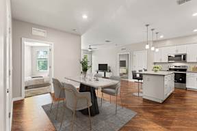 Open-concept kitchen and dining with island, stainless appliances, marble table, and wood floors.
