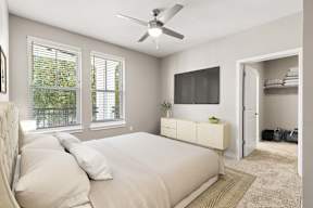 Staged bedroom with bed, ceiling fan, wall TV and walk-in closet at The Flats at Tioga Town Center.