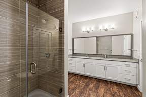 Glass-enclosed walk-in shower and double-sink vanity in a modern bathroom at The Flats at Tioga Town Center.