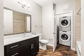 Bathroom with dark vanity, hardwood-style floors and stacked washer/dryer in a closet in an apartment in Newberry, FL.