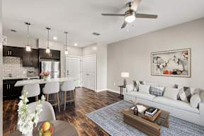 Stylish open-concept living area with kitchen island, three bar stools, sofa, and wood floors at Flats at Tioga Town Center's apartments in Newberry, FL.