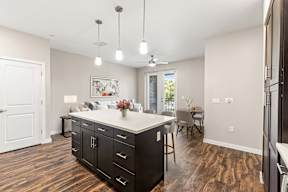 Open-plan kitchen with dark island, pendant lights, dining area and balcony at The Flats at Tioga Town Center.