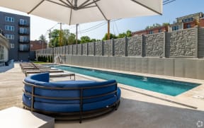 a pool with a blue couch and lounge chairs and a gray stone wall in the background