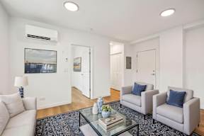 A living room with a white couch, two grey armchairs, a glass coffee table, and a painting on the wall.