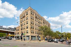 A large tan building with a flat roof and a street in front of it.