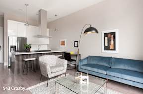 a living room with a blue couch and a kitchen with a bar and a lamp