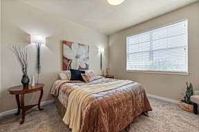 A bedroom with a bed, a table, and a painting on the wall.