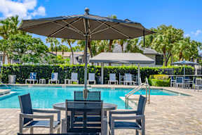A table with chairs and an umbrella is in front of a pool.