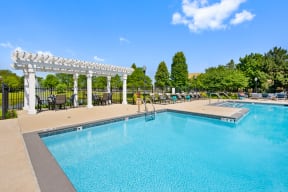 Apartments for Rent in Naperville, IL - 803 Corday at Naperville - Resort Style Outdoor Pool With Pergola Seating, Lounge Chairs, Sun Deck, And Fenced Courtyard Surrounded By Green Trees.
