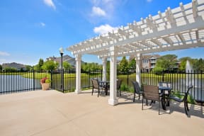 Apartments in Naperville IL - 803 Corday at Naperville - Outdoor Patio With Black Fence, Pond View, Table With Chairs, And White Wood Shading.