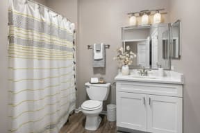 Two-Bedroom Apartments in Naperville, IL - 803 Corday at Naperville - Bathroom with Wood-Style Flooring, White Cabinets, Toilet, Mirror, and Shower Curtain.