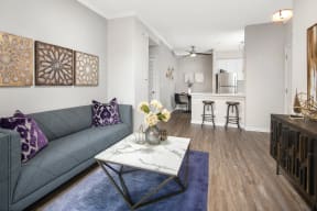 One-Bedroom Apartments in Naperville, IL - 803 Corday at Naperville - Living Room with Wood-Style Flooring, Area Rug, Couch, Coffee Table, and View of Kitchen and Dining Area.