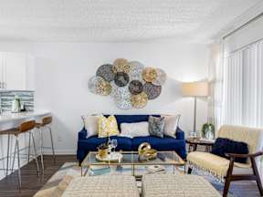 A blue couch with a yellow throw pillow sits in a living room with a coffee table in front of it.