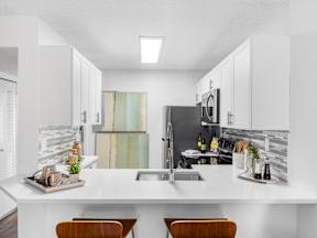 A modern kitchen with a white countertop and wooden chairs.