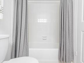 A white bathroom with a white tub and grey curtains.