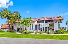 A white house with a red tile roof and a blue sign in front.