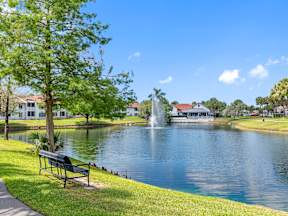 A serene park with a bench, a fountain, and a clear blue sky.