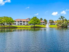 A serene lake with a fountain in the middle of it and a building in the background.