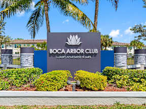 A sign for Boca Arbor Club in front of some trees.
