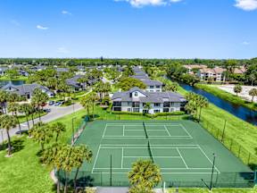 A tennis court is surrounded by houses and palm trees.