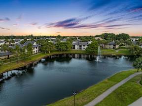 A serene lake surrounded by houses with a fountain in the middle.