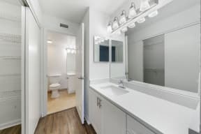 Bathroom with linen closet, sink, cabinets and lighting looking into separate room with toilet