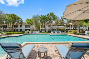 a swimming pool with chairs and umbrellas in front of an apartment building