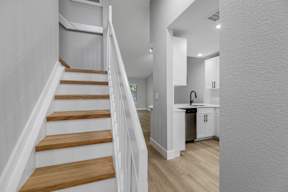 A staircase with wooden steps and white railings leads to a kitchen area.
