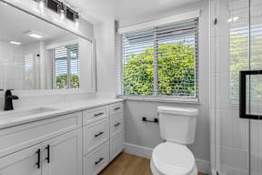 A white toilet in a bathroom with a window overlooking a green tree.