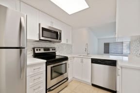 Kitchen with cabinets, stainless steel refrigerator, oven, microwave, dishwasher, sink with vegetable sprayer and pass-through into living room