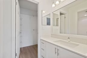Bathroom with cabinets, sink, mirror, medicine cabinet, and lighting looking into walk-in closet
