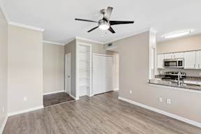 A room with a ceiling fan and a kitchenette in the corner.