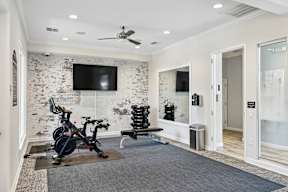 A room with a bicycle on a mat in front of a brick wall and a ceiling fan.