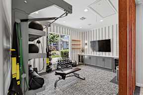 A gym room with a bench, weights, and a television.